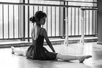 一张黑白照片 一个年轻女孩坐在舞蹈工作室的地板上 抬头看着地板。