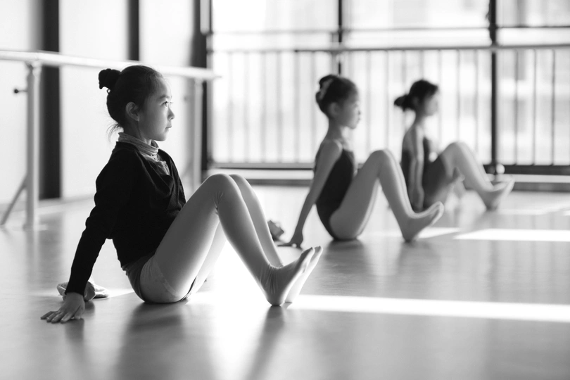 一些小女孩坐在地板上 在一个舞蹈工作室里 穿着黑色和白色服装的年轻舞者。