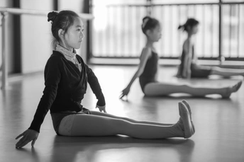 一个小女孩在一个芭蕾舞课上坐在地板上 其他年轻的舞者坐在她身后。