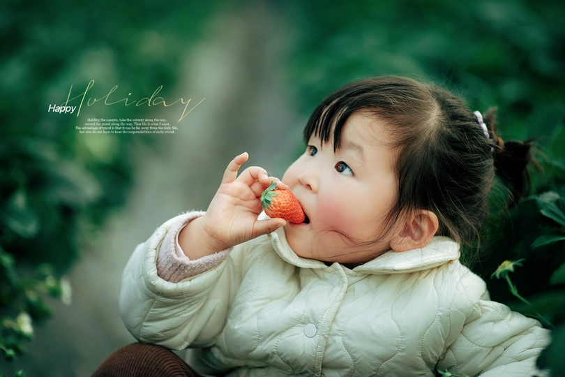 一个小女孩手里拿着一个草莓 嘴里含着一根胡萝卜。