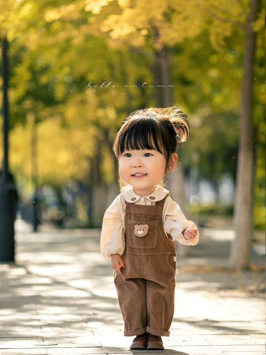 一个小女孩穿着工装裤站在公园人行道上