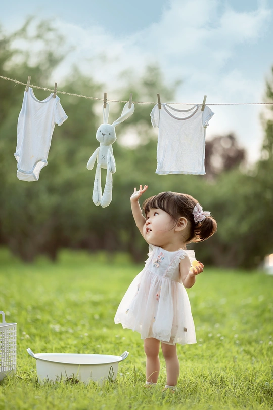 一个小女孩穿着白色连衣裙站在草地上 晾衣绳上晾着衣服。