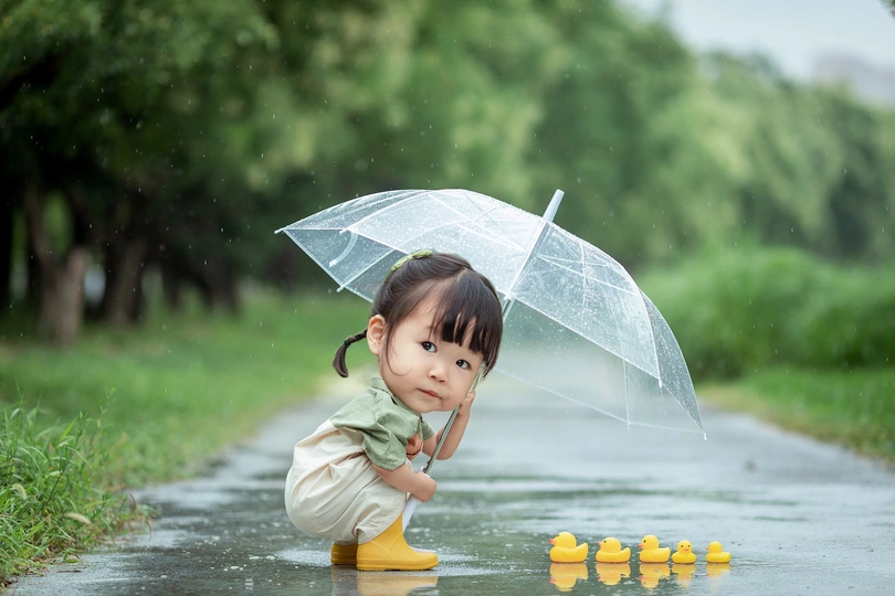 一个小女孩在雨中玩水坑 带着一把透明的雨伞