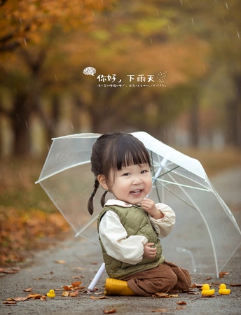 一个小孩子拿着一把透明的雨伞坐在雨中