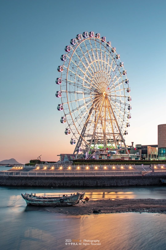 夕阳下 俯瞰城市的巨大的 Ferris 轮 河上有一艘船。