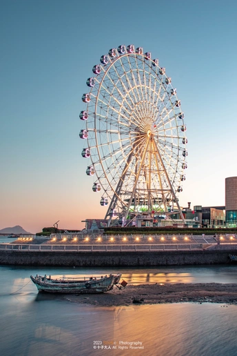 夕阳下 俯瞰城市的巨大的 Ferris 轮 河上有一艘船。