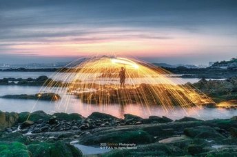 一张男子站在岩石上 太阳照亮了水面 海面泛起金光的照片。