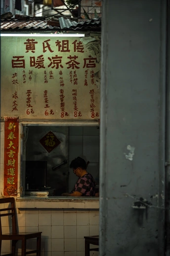 一位坐在建筑物前窗边的桌子上的女人 上面有标志。