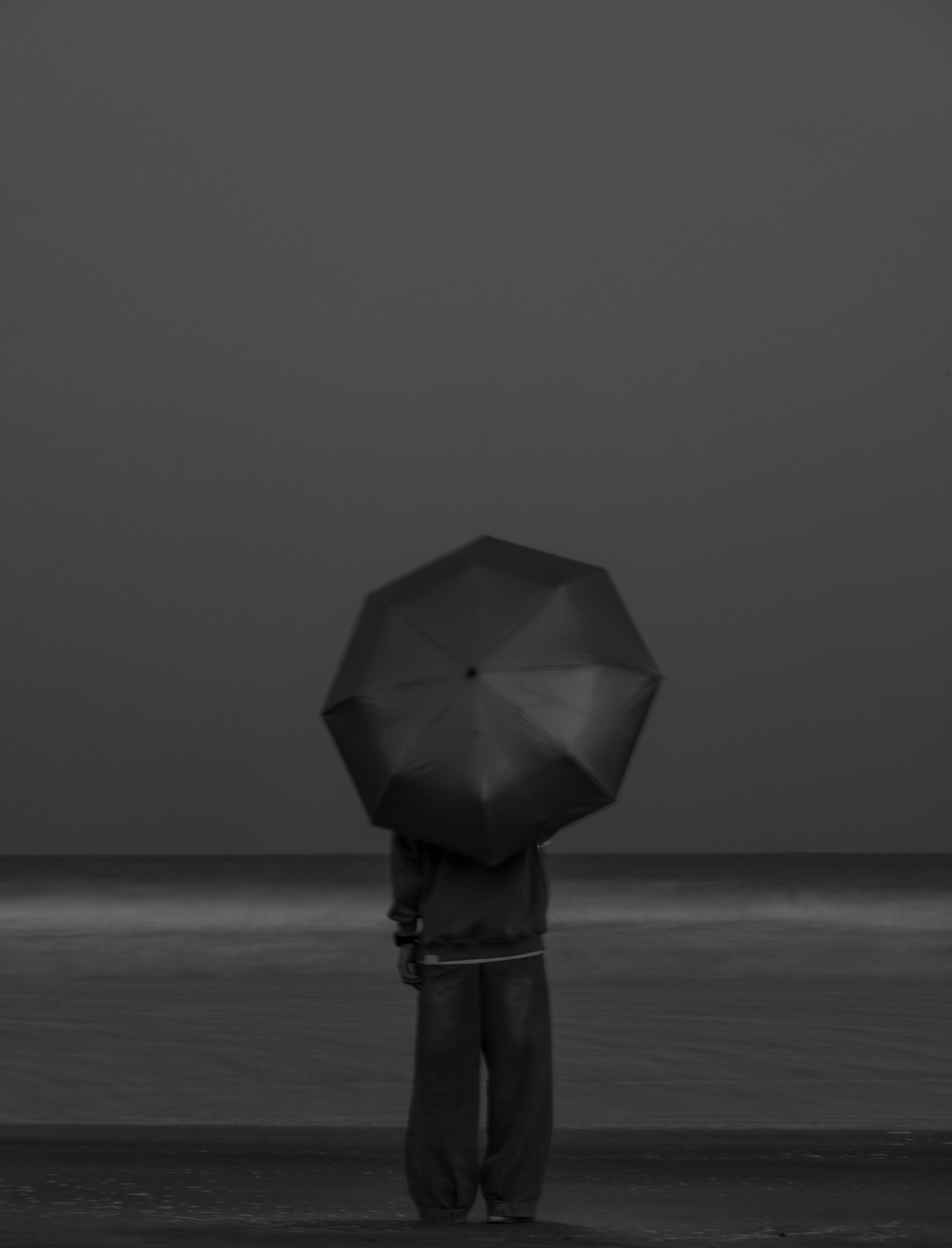 一个人站在沙滩上 手里拿着一把黑色的雨伞。