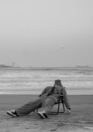 一张黑白照片 一个男子躺在沙滩上的椅子上 另一个人在沙滩上 带着一把伞和一把伞。