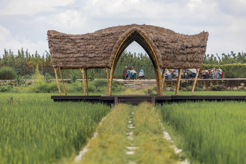 一群人在一个绿色的草地上站在一个有茅草顶的凉亭前面。