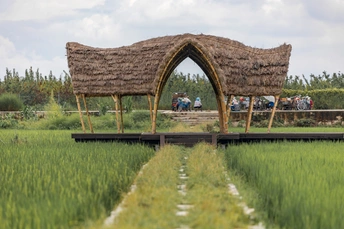 一群人在一个绿色的草地上站在一个有茅草顶的凉亭前面。