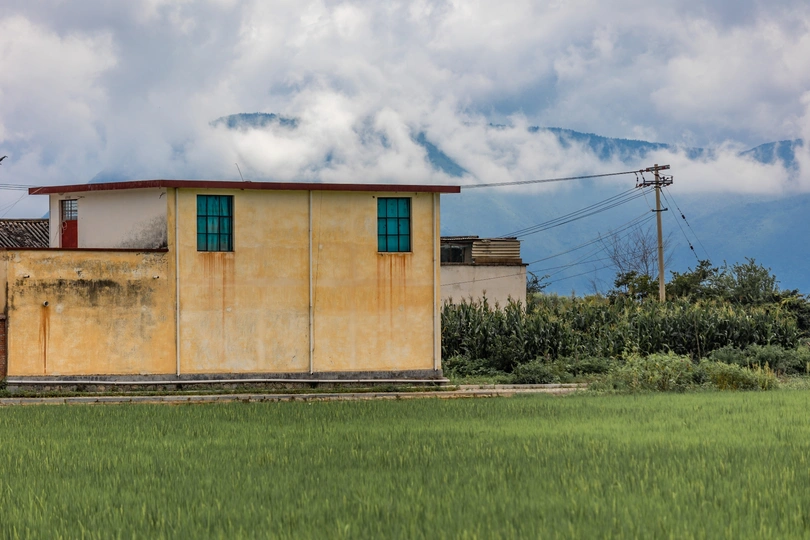 背景是山和云的绿色草地上有一座黄色房子