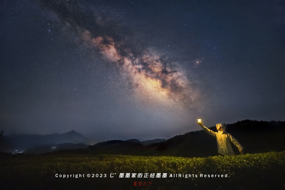 一个人在夜晚伸出手臂仰望天空 背景中出现了银河。