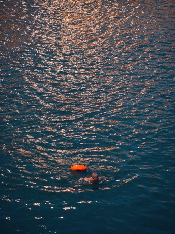 夕阳下在海洋中游泳的男子手里拿着一个橙色球