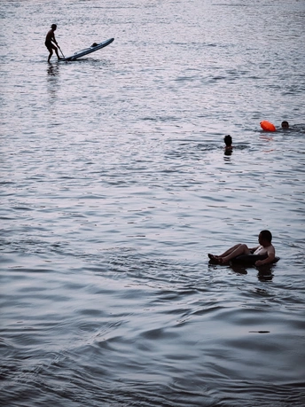 一个坐在冲浪板上漂浮在水中的男子 周围有人在海里游泳。