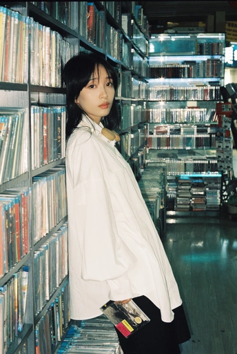 一个穿着白衬衫的女人站在装满cd和dvd的架子前