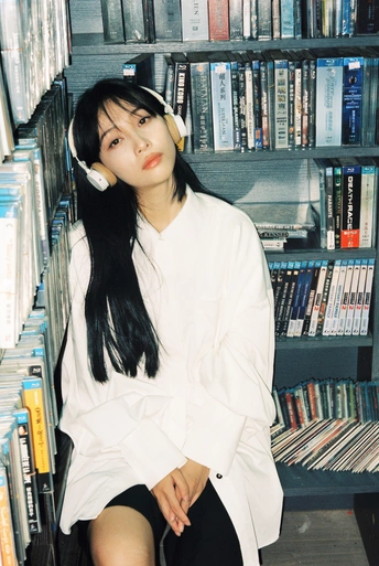 一个戴着白色耳机的年轻女子坐在书架上放满cd的图书馆里