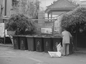 一张黑白照片 一位男子站在街边的垃圾箱旁边 旁边还有一只狗。