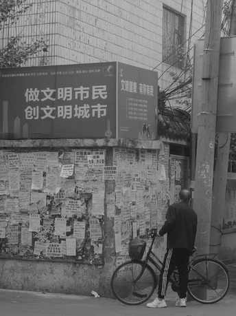 一个穿着黑白衣服的男子走在一条街道上 经过一面有海报和标志的墙。