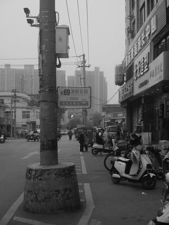 一张黑白照片 展示了一个亚洲城市的街道 街道上有骑摩托车和摩电车的人。