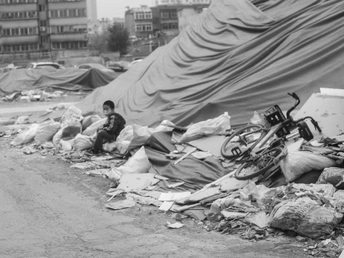 一张黑白照片 展示了一个城市街道 有帐篷、摩托车、女人、孩子和垃圾以及其他碎片。
