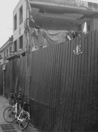 一张黑白照片 街道上有一道围墙 一座建筑 一辆自行车靠在墙上