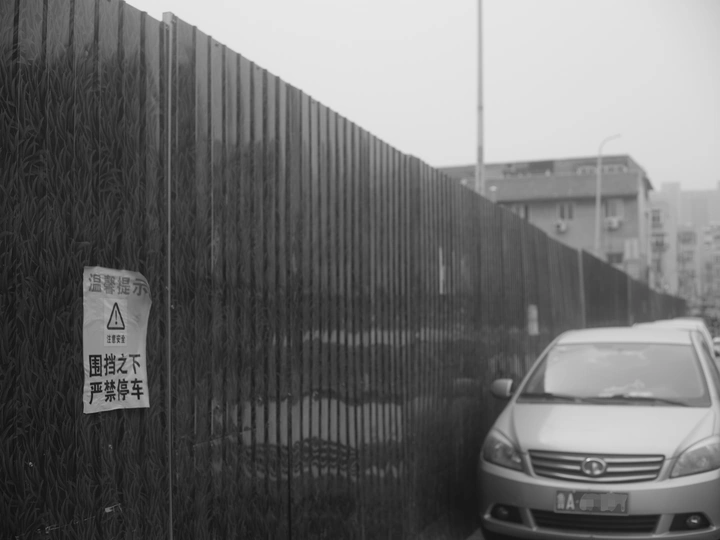 路边停着一辆车 旁边有一堵墙 墙上有一个标志。