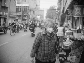 一张黑白照片 一个人戴着口罩走在一条拥挤的街道上。