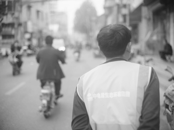 一张黑白照片 一个骑自行车的人在街道上 还有其他人在摩托车上。