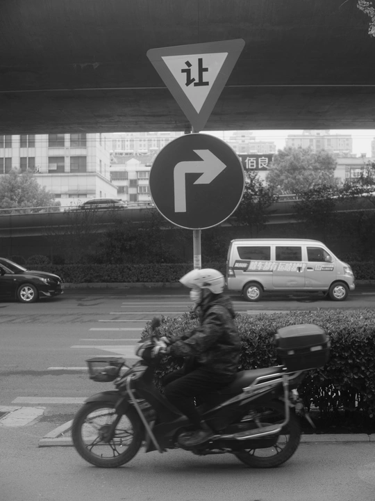 一张黑白照片 描绘了一个骑摩托车的人在路口与行驶中的汽车 