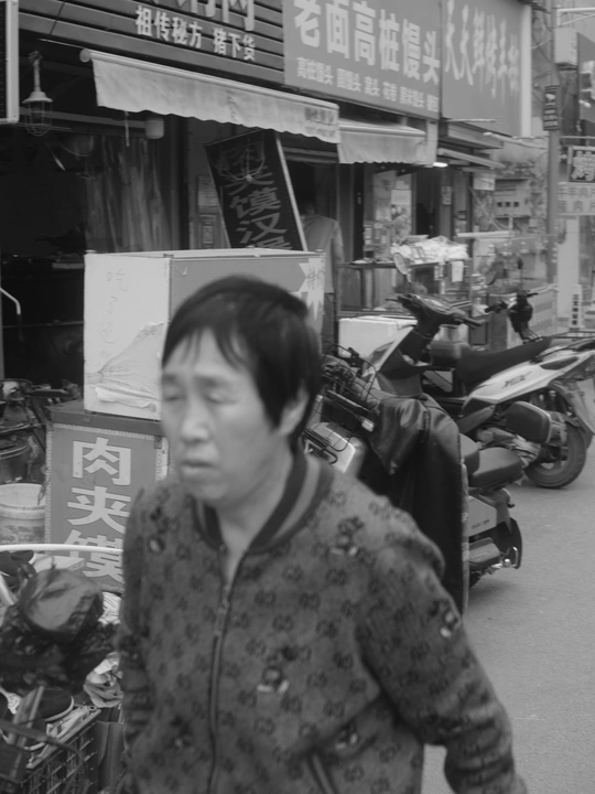 一张黑白照片 一位女士走在靠近商店的街道上。