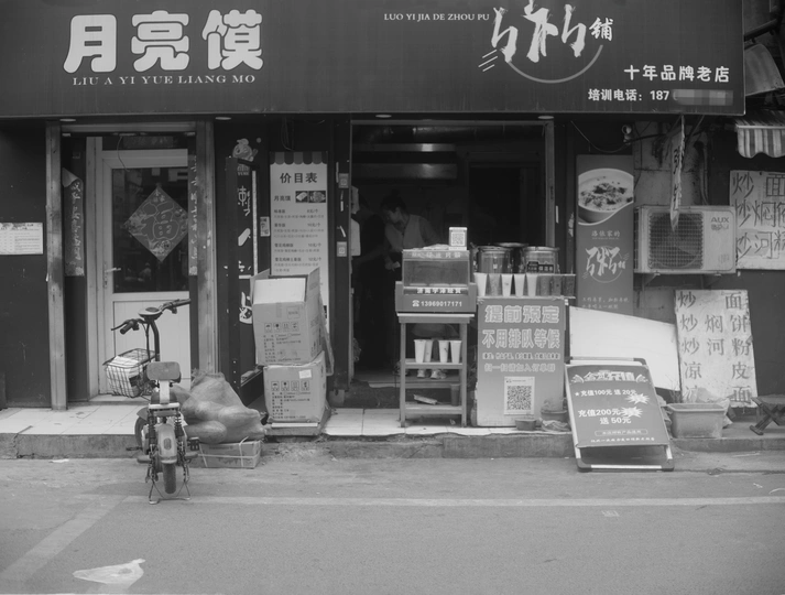 一张黑白照片 展示了一家商店的正面 一辆自行车停在商店前面 一座带有中文招牌的建筑。