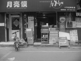 一张黑白照片 展示了一家商店的正面 一辆自行车停在商店前面 一座带有中文招牌的建筑。