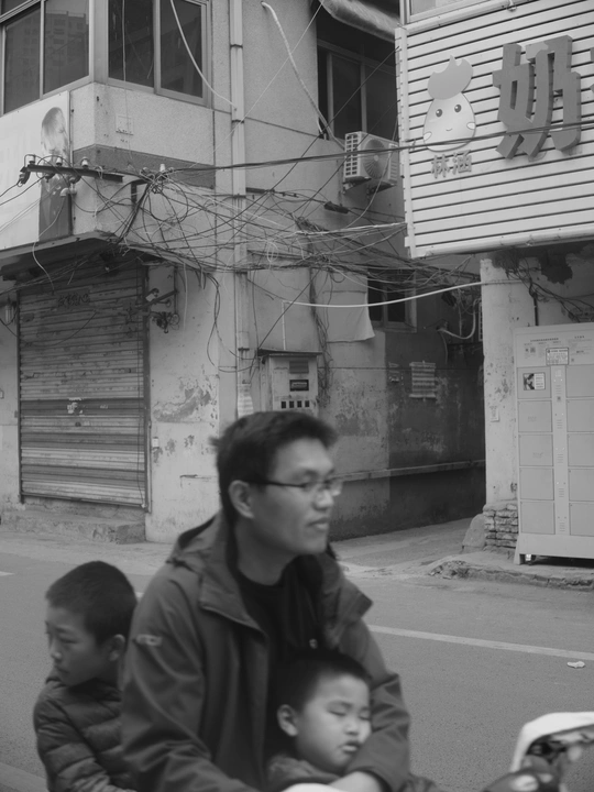 一个男孩骑在摩托车上 摩托车旁边有一栋建筑 男孩在摩托车前面。