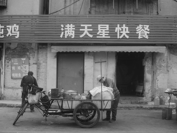 一张黑白照片 一个男人推着一辆小车在街上走。