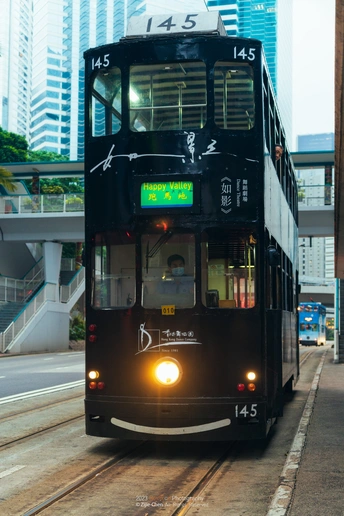 一辆黑色双层公交车在城市街道上行驶 背景是建筑物和轨道上的火车。