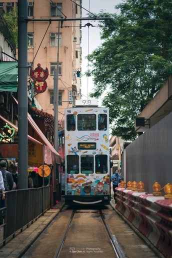 双层公交车沿着狭窄的街道行驶 街道上有人和火车在轨道上。