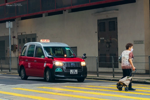 一个推婴儿车的人带着他的狗过马路 一辆红色的汽车开过来。
