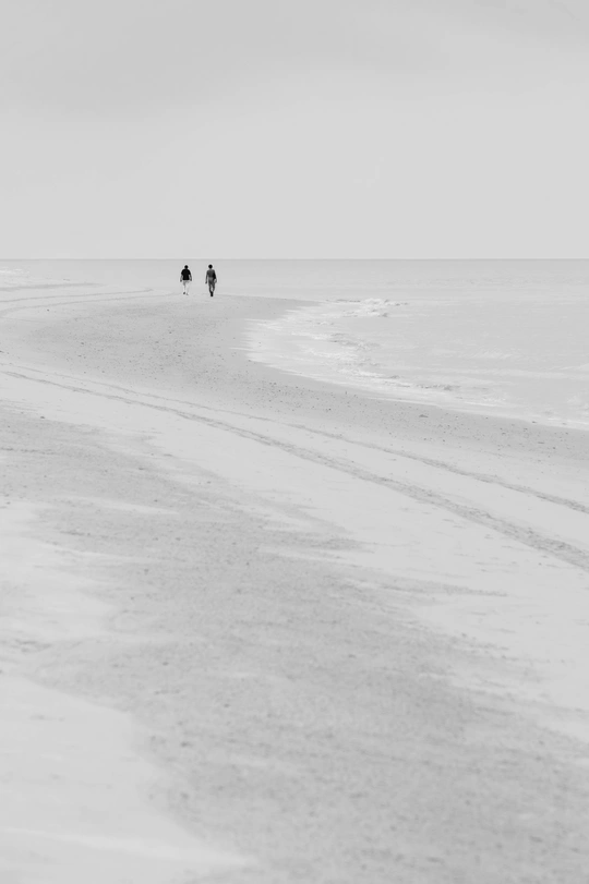 一个人骑着马在靠近海洋的沙滩上行走 而另一个人拿着伞在远处走。