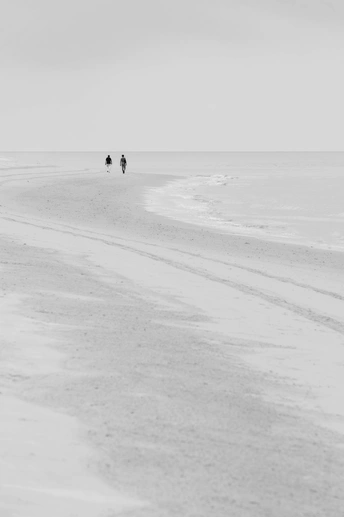 一个人骑着马在靠近海洋的沙滩上行走 而另一个人拿着伞在远处走。