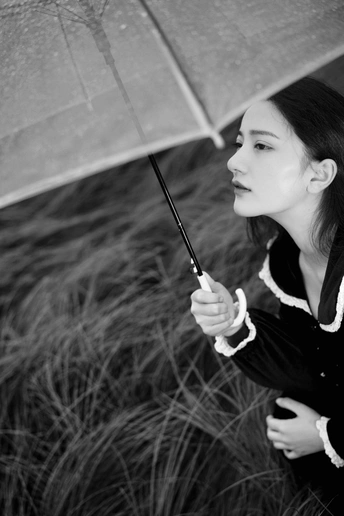 一位年轻女子手持雨伞站在一片高草地上