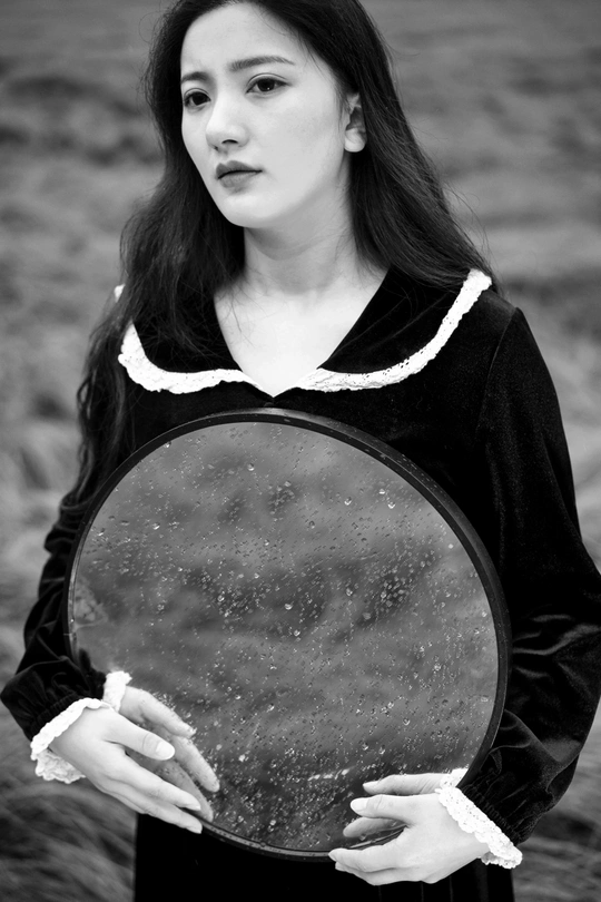 一张黑白照片 一位年轻女子穿着裙子 手里拿着镜子