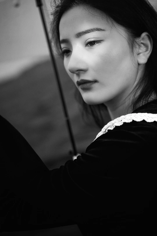 一张黑白照片 一位年轻女子手持雨伞 向左看。