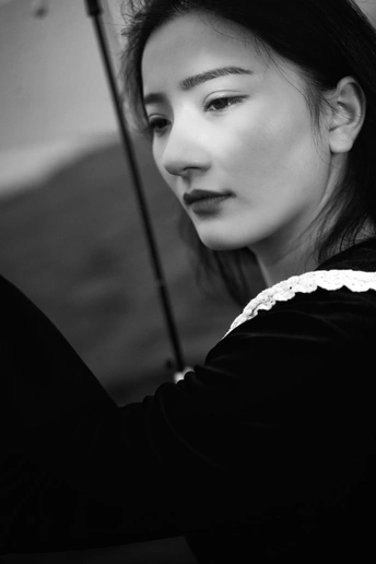 一张黑白照片 一位年轻女子手持雨伞 向左看。