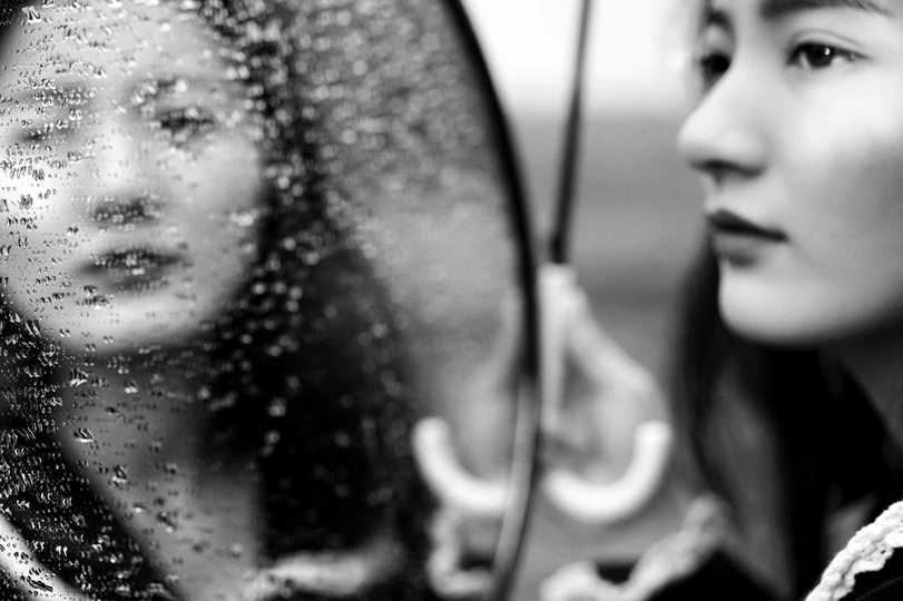 一张黑白照片 一个年轻女孩正看着镜子里的自己的倒影。