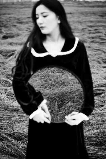 一个穿着黑色连衣裙的年轻女子 手提着旅行箱站在一片高草丛中。