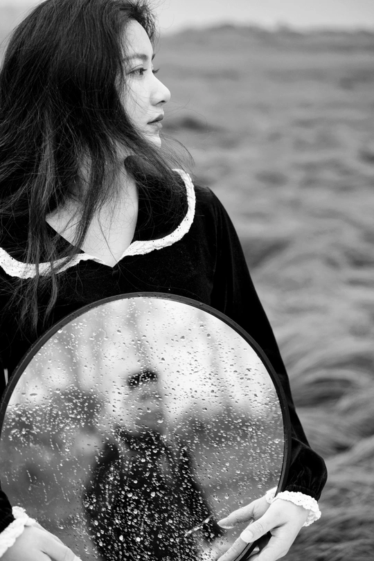 一张黑白照片 一位年轻女子举着镜子照镜子 镜子里有水在后面。