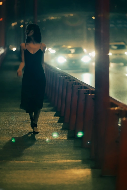 一位穿着黑色连衣裙的女人在夜晚走过一座桥。