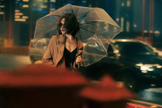 一位年轻女子在晚上城市街道上拿着一把透明的雨伞走下来